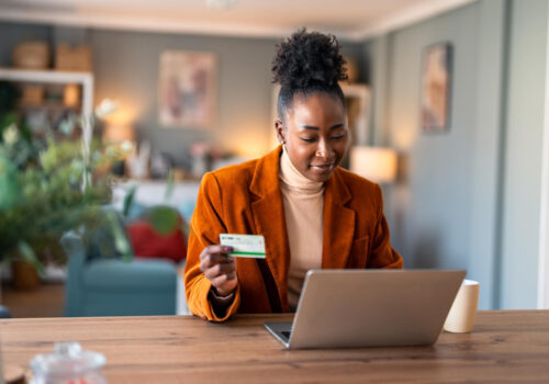 Woman shopping online on her laptop while holding a credit card at her desk.